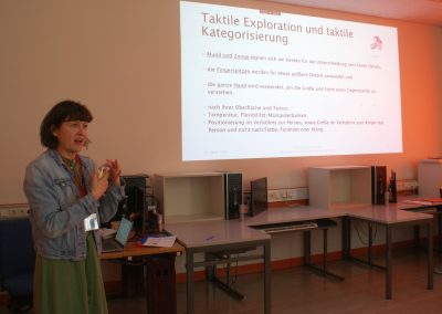 Workshop 12 von Mag. Horkava. Die Referentin steht vorne im Workshop-Raum und ist gerade dabei etwas zu beschreiben. Neben ihr wird ihre Präsentation an die Wand projiziert.